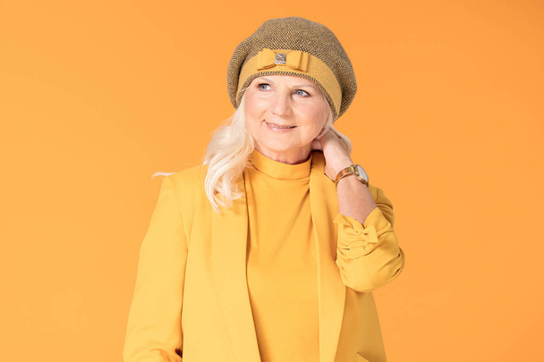 Smiling mature woman in yellow beret posing in studio. - Foto, afbeelding