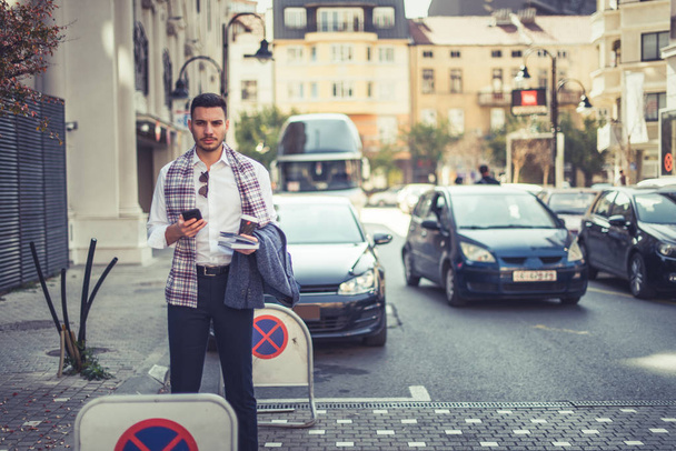 Молодой городской бизнесмен стоит на улице, смотрит вперед, в то время как позади него много машин
 - Фото, изображение