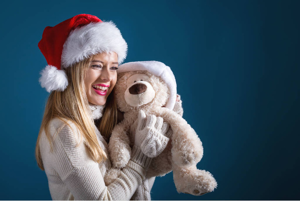 Young woman with santa hat holding a teddy bear - Фото, изображение