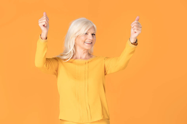 Attrative smiling fashionable senior woman posing on yellow studio background. - Fotoğraf, Görsel