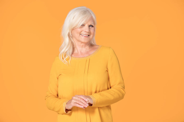 Attractive smiling fashionable senior woman posing on yellow studio background. - Foto, afbeelding