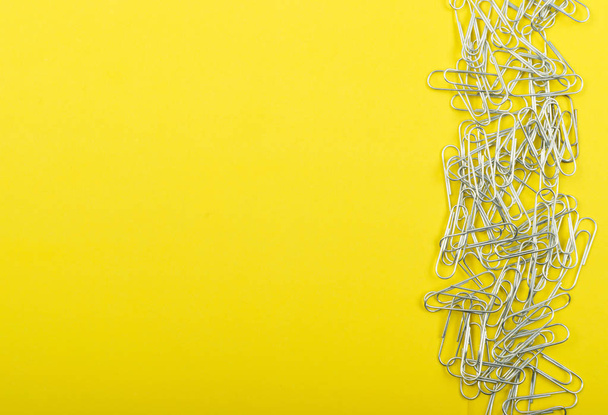Heap of note paper clips on yellow background top view. Pile of steel clips or paperclips with copyspace - Фото, изображение
