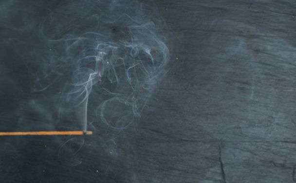 brennende indische Räucherstäbchen mit Rauch auf schwarzem Steinhintergrund. duftende rauchige Sandelholz Stick Draufsicht - Foto, Bild