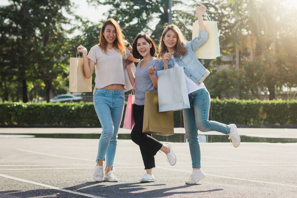 Group of young Asian woman shopping in an outdoor market with shopping bags in their hands. Young Asian women show what they got in shopping bag under warm sunlight. Group outdoor shopping concept. - Photo, Image