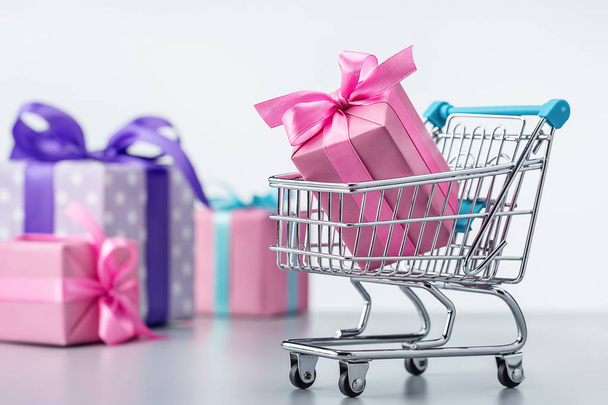 Shopping cart with gift box in pink packaging. Gifts in multi-colored packaging, decorated with ribbons and bows. - Photo, Image