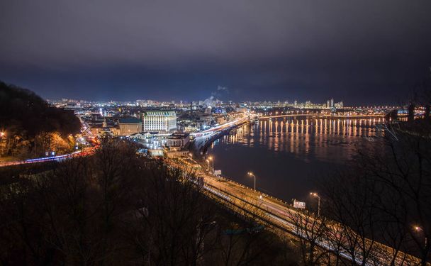 Panorama of night city landscape with river and bridge. Reflection of glowing lanterns in water - Foto, Bild