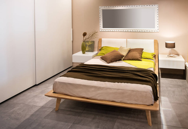 Dormitorio moderno con cama de estilo escandinavo de madera y armarios laterales en decoración beige y gris con cojines de acento amarillo en el diván
 - Foto, Imagen