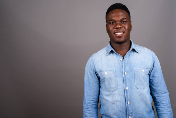 Νεαρός Αφρικανός που φοράει denim πουκάμισο σε γκρι φόντο - Φωτογραφία, εικόνα