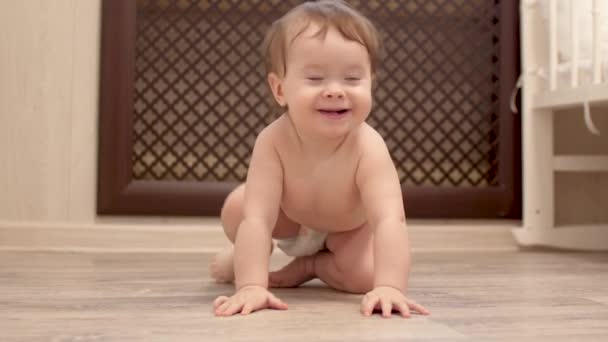 Happy little baby in diaper is learning to crawl on floor and smiling - Footage, Video