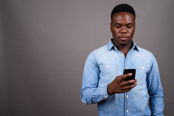 Joven africano usando teléfono móvil contra fondo gris - Foto, imagen