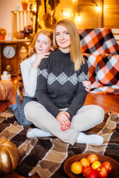 Red-haired teen girl and her mom in the studio in the fall scenery with yellow leaves, blankets, apples and pumpkins - Foto, Bild