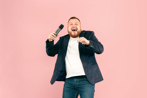 junger Mann mit Mikrofon auf rosa Hintergrund, der mit Mikrofon führt - Foto, Bild