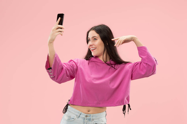 Portrait of a happy smiling casual girl showing blank screen mobile phone isolated over pink background - Foto, Imagen