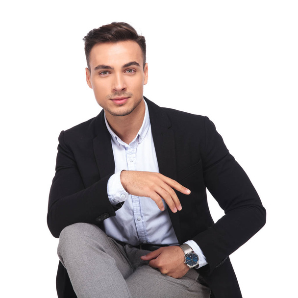 portrait of handsome businessman resting hand on knee while sitting on white background - Fotografie, Obrázek