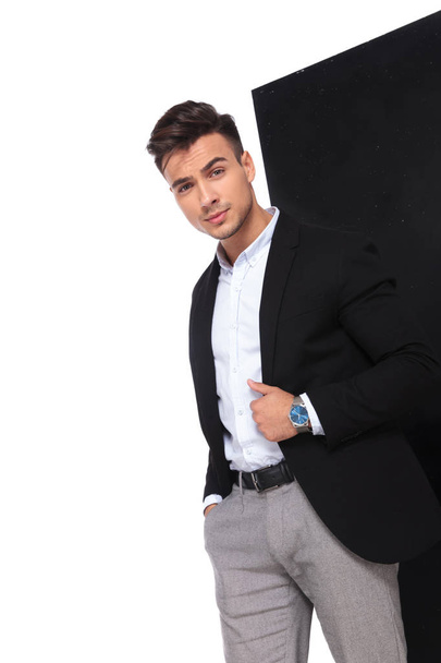 portrait of young businessman holding pocket and black suit collar while standing on black and white background - Фото, изображение