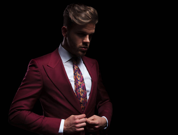 side view of a dramatic young businessman buttoning his suit on black background - Photo, Image