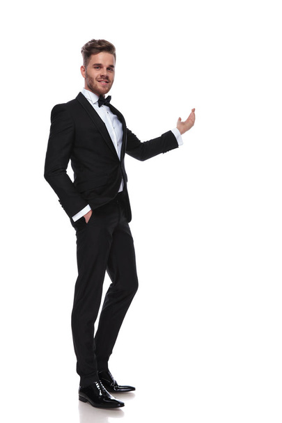 elegant man in tuxedo presenting something on white background - Zdjęcie, obraz