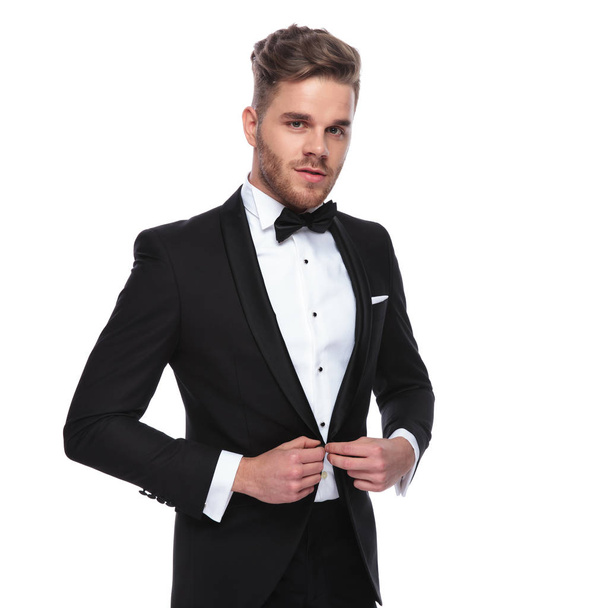 young elegant man buttoning his tuxedo on white background - Photo, Image