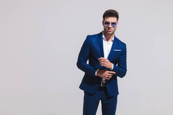 fashion sexy man in suit and sunglasses fixes his sleeve on grey background - Photo, Image