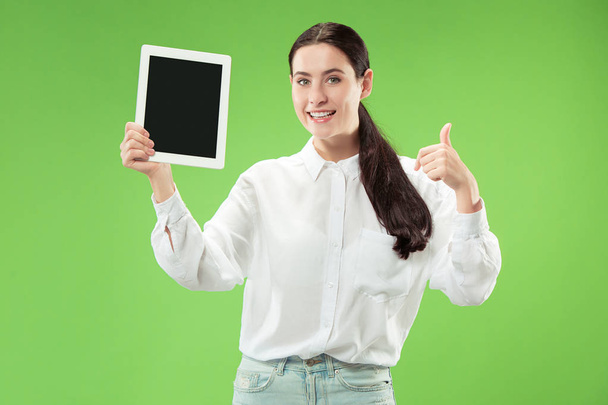Portrait of a confident casual girl showing blank screen of laptop isolated over green background - Foto, Imagen