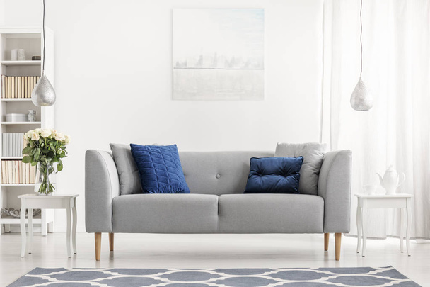Blue pillows on grey couch next to table with flowers in white flat interior with painting. Real photo - Fotoğraf, Görsel