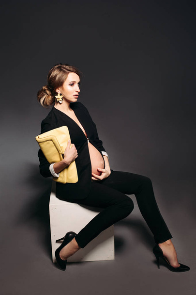 Elegant pregnant woman sitting against black studio background. - Фото, зображення