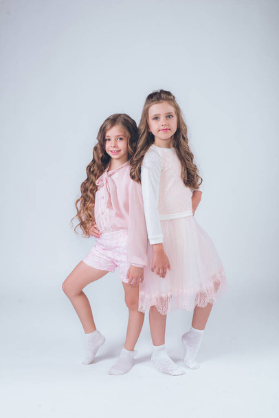 niedliche kleine Mädchen mit lockigem Haar in modischen Kleidern in weiß und rosa im Studio - Foto, Bild