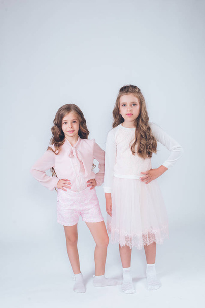 Cute little girls with curly hair in fashionable clothes of white and pink in the studio - Foto, imagen