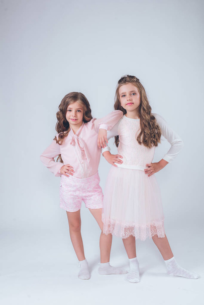 Cute little girls with curly hair in fashionable clothes of white and pink in the studio - Valokuva, kuva