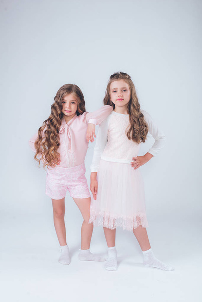 Cute little girls with curly hair in fashionable clothes of white and pink in the studio - 写真・画像