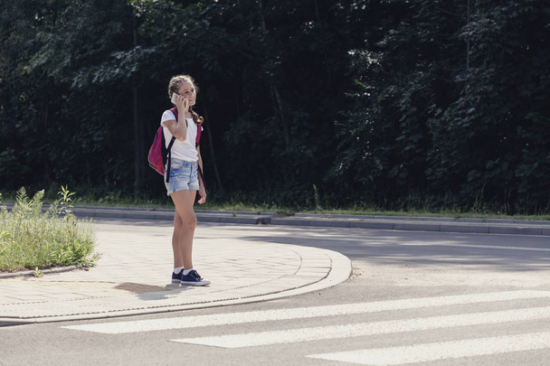 Teenager schoolgirl talking on the phone and walking in pedestrians crossing - Zdjęcie, obraz
