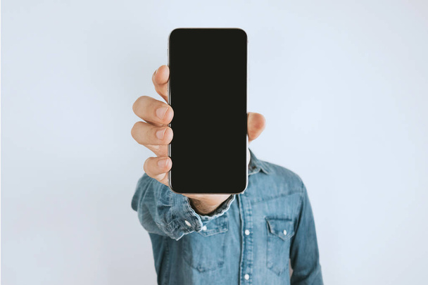 Porträt eines Mannes im Jeanshemd. zeigt ein Smartphone vor der Kamera. grauer Hintergrund. - Foto, Bild