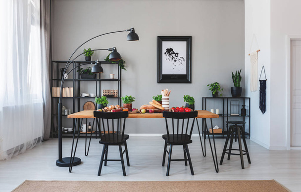 Black chairs and lamp at wooden table with food in grey dining room interior with poster. Real photo - Foto, Imagem