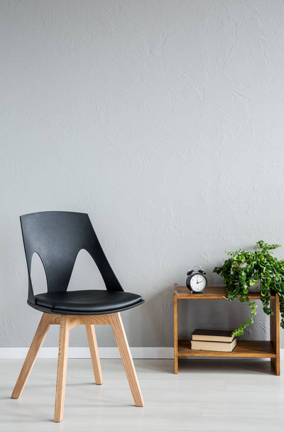 Elegant black wooden chair next to cabinet with clock and flowers in modern office interior, real photo with copy space on the empty wall - Foto, afbeelding
