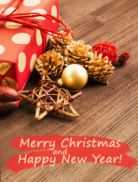 Decoración festiva de Navidad y Año Nuevo, bolas rojas y doradas, conos de abeto y estrellas con regalo envuelto en papel rojo con círculos dorados sobre fondo de madera marrón con texto Feliz Navidad y Feliz Año Nuevo
 - Foto, Imagen
