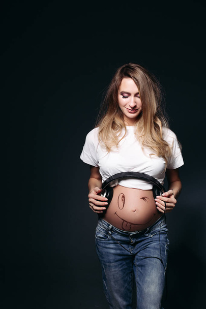 Усміхнена вагітна жінка з великими навушниками на животі
. - Фото, зображення