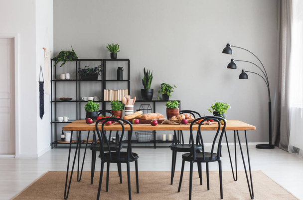 Black chairs and wooden table with food on brown carpet in grey dining room interior. Real photo - Fotó, kép