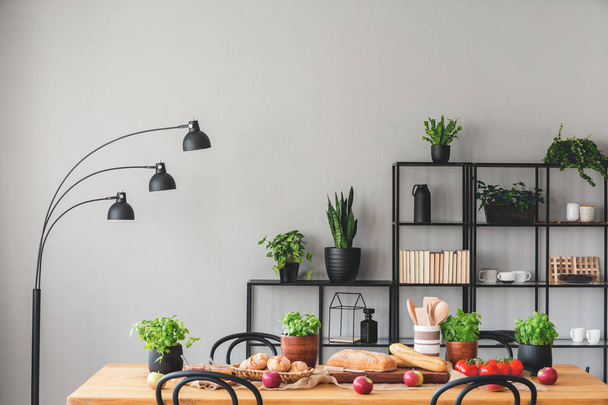 Basil and apples on wooden table in grey dining room interior with lamp and plants on shelves. Real photo - Foto, Bild