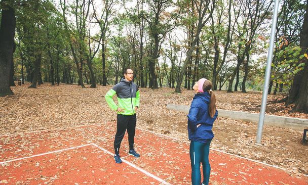Sporty man and woman doing warm up exercise at park. Fit young couple training in autumn morning in nature. - 写真・画像