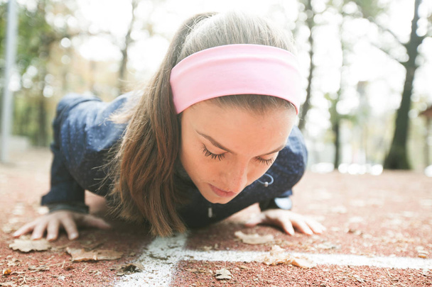 Nuori urheilullinen nainen tekee punnerruksia ulkona kuntoilupuistossa syksyllä aamulla
. - Valokuva, kuva