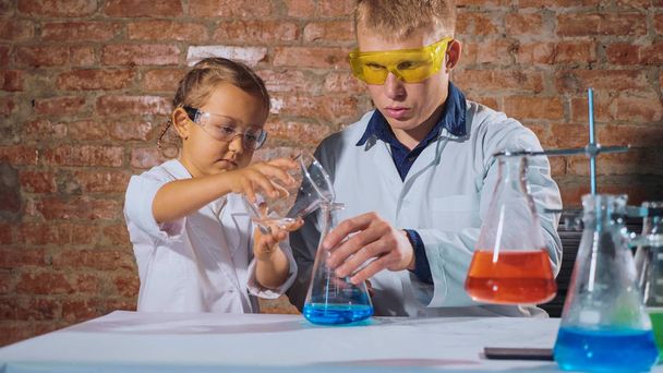 Mężczyzna naukowiec z niewiele uczennica prowadzi eksperyment chemiczny razem - Zdjęcie, obraz