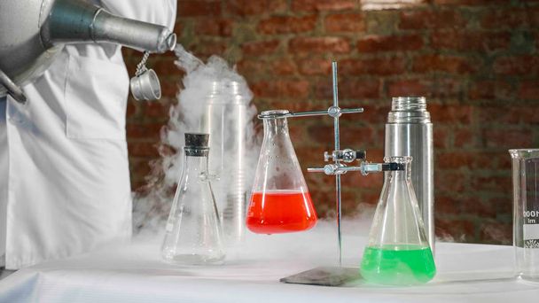 Scientist pouring liquid nitrogen in steel thermos bottle at laboratory - Foto, afbeelding