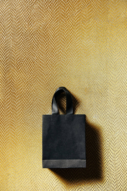top view of black shopping bag on golden background, black friday concept - Фото, изображение