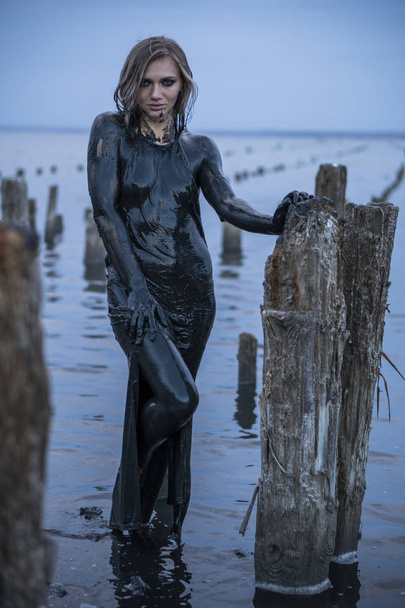 Ritratto di ragazza caucasica bionda rimane spalmata in un fango nero sano in vecchio Firth con messaggi di legno per la produzione di sale
 - Foto, immagini