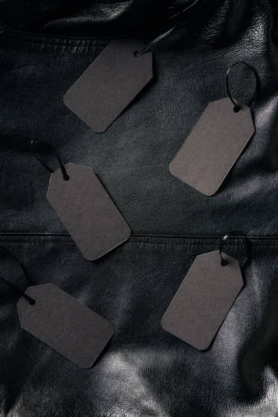 top view of arranged blank price tags on black leather jacket background, black friday concept - Foto, imagen