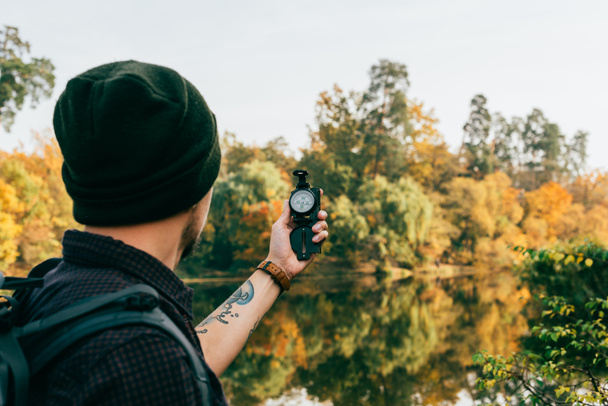male traveller with backpack holding compass on autumnal background - Foto, imagen