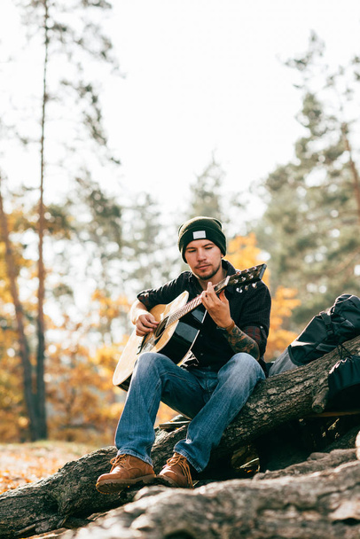 дорослий чоловік грає на акустичній гітарі, сидячи на дереві в парку
  - Фото, зображення