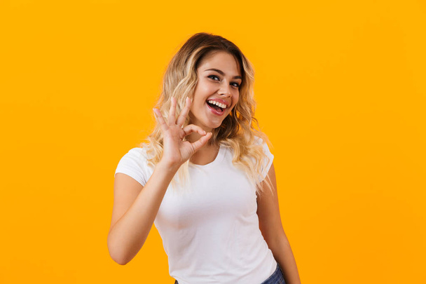 Photo of pretty blond woman in basic clothing smiling and showing ok sign isolated over yellow background - Valokuva, kuva