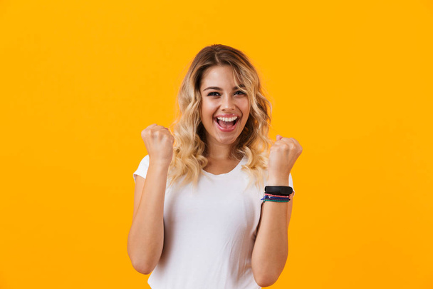 Photo of joyous woman in basic clothing screaming and clenching fists isolated over yellow background - Фото, зображення