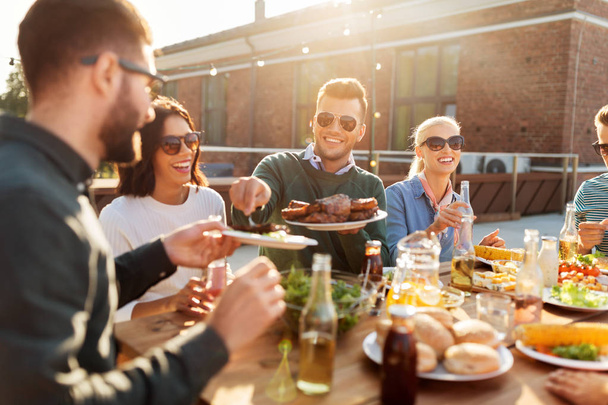 happy friends eating at barbecue party on rooftop - 写真・画像